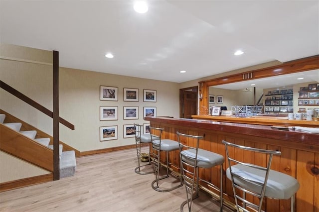 bar with stairs, baseboards, recessed lighting, a bar, and light wood finished floors