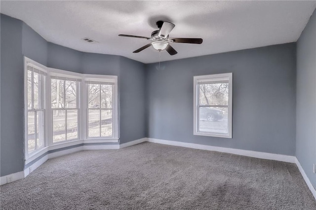 empty room with carpet floors, visible vents, baseboards, and a ceiling fan