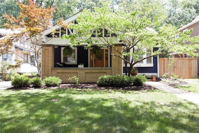 bungalow-style house with a front yard, covered porch, brick siding, and fence