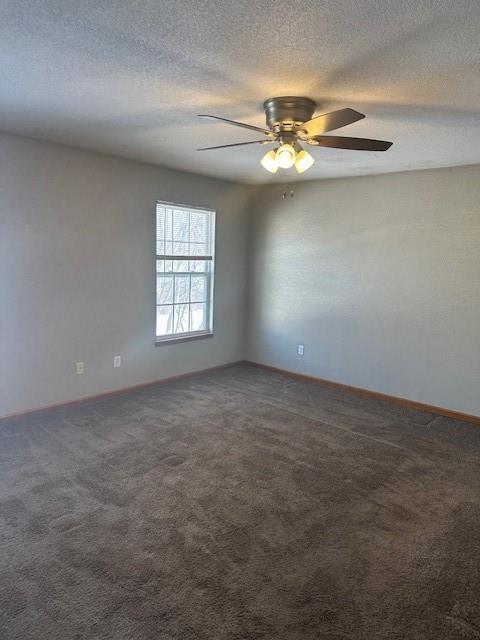 spare room featuring a textured ceiling, dark colored carpet, ceiling fan, and baseboards