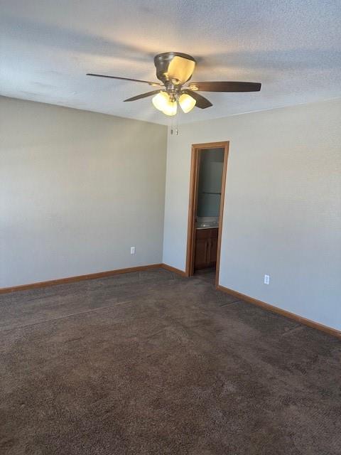 spare room with a ceiling fan, dark colored carpet, a textured ceiling, and baseboards