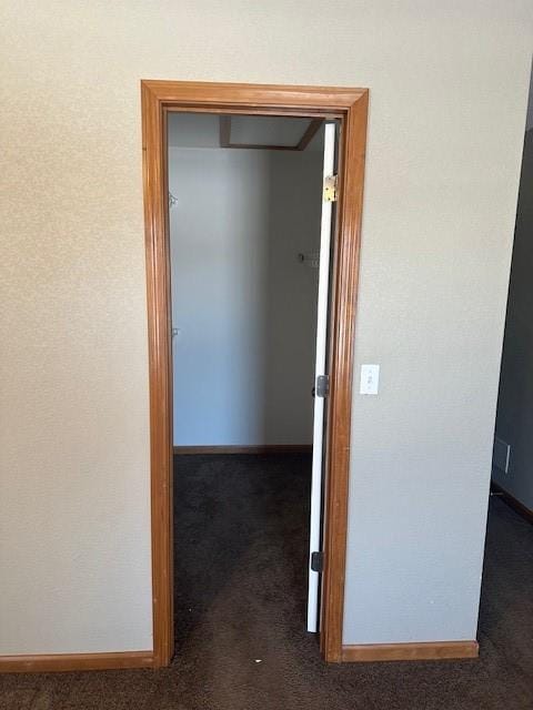 hallway featuring dark colored carpet and baseboards