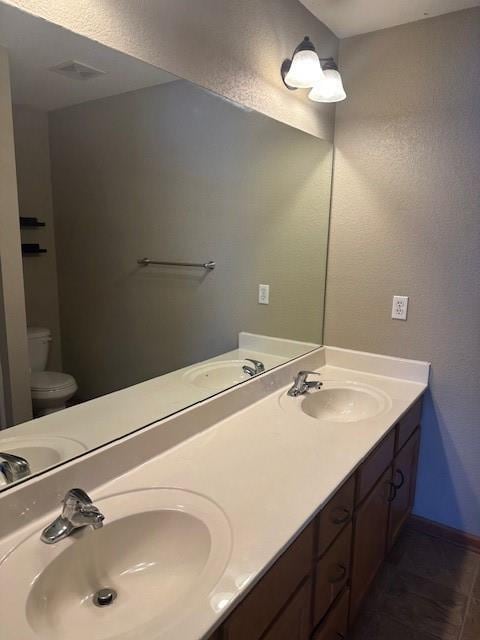 full bathroom featuring baseboards, a sink, toilet, and double vanity