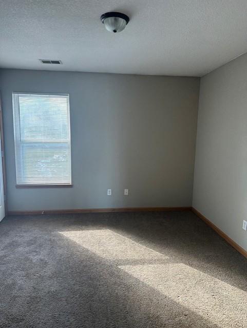 carpeted empty room with baseboards, visible vents, and a textured ceiling