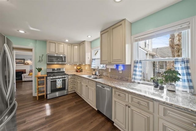 kitchen featuring cream cabinets, stainless steel appliances, a sink, dark wood-style floors, and tasteful backsplash