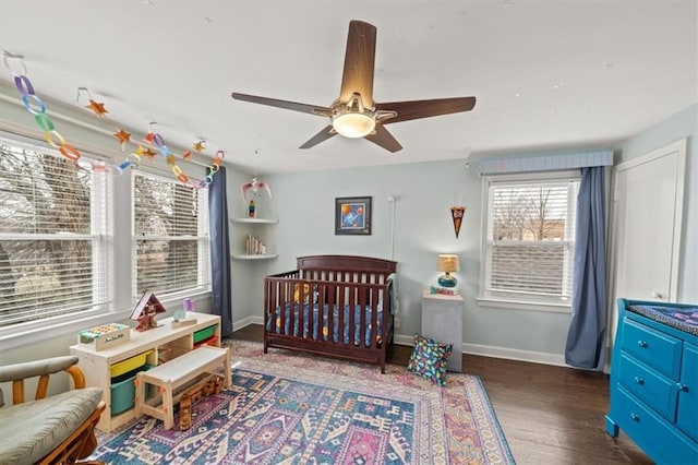 bedroom featuring a nursery area, wood finished floors, a ceiling fan, and baseboards