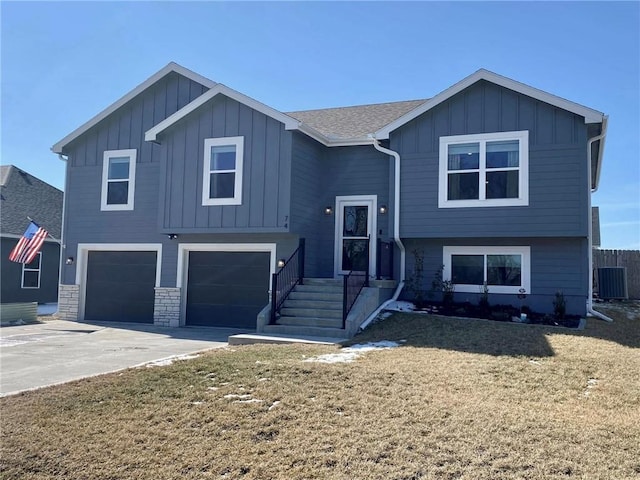 raised ranch featuring central AC unit, an attached garage, concrete driveway, stone siding, and board and batten siding