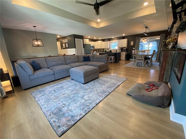 living room with light wood-type flooring, a tray ceiling, recessed lighting, and a ceiling fan