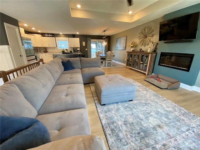 living room featuring light wood finished floors, recessed lighting, a raised ceiling, and baseboards