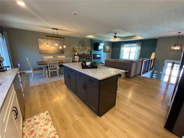 kitchen with open floor plan, light stone counters, light wood-type flooring, and decorative light fixtures