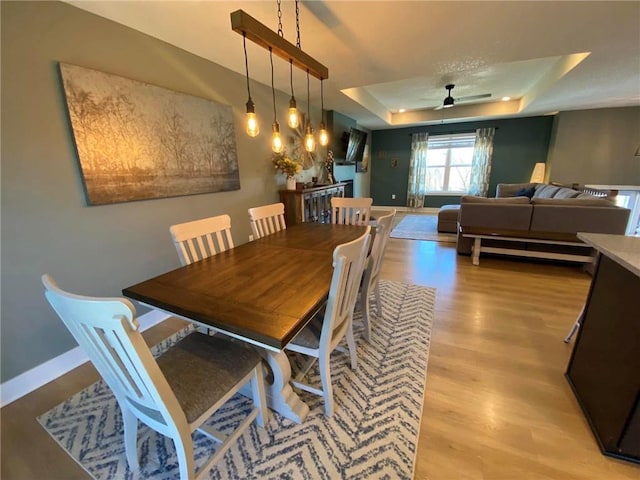 dining area featuring light wood finished floors, a tray ceiling, a ceiling fan, and baseboards