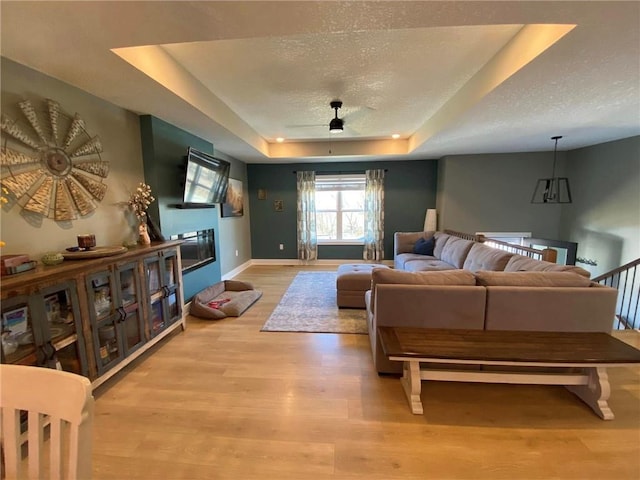 living room with light wood-type flooring, a raised ceiling, a glass covered fireplace, and a textured ceiling