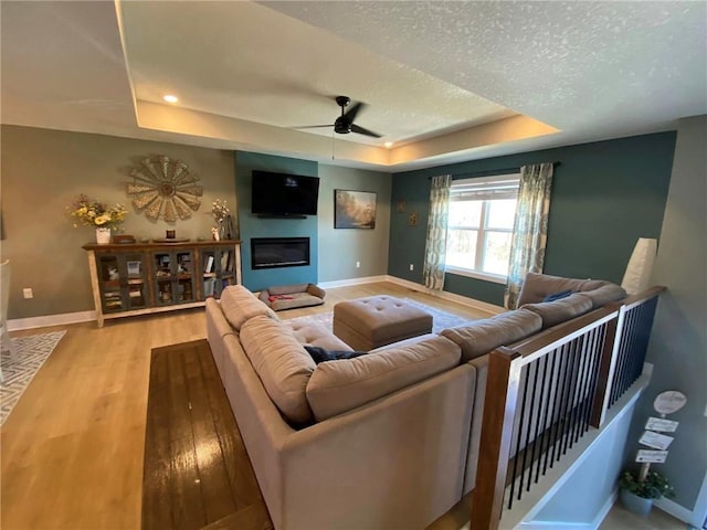 living area with a tray ceiling, baseboards, a glass covered fireplace, and light wood finished floors