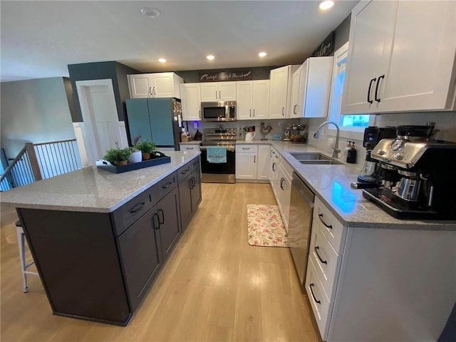 kitchen featuring a sink, light wood-style floors, white cabinets, appliances with stainless steel finishes, and a center island