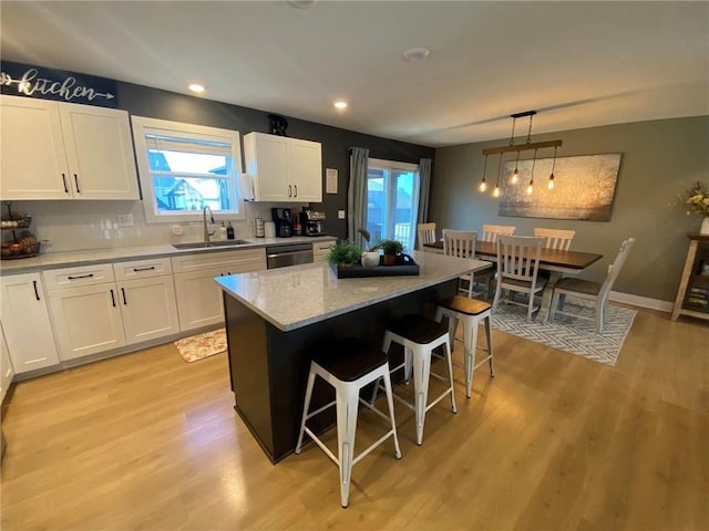 kitchen featuring hanging light fixtures, stainless steel dishwasher, white cabinetry, a kitchen island, and a sink