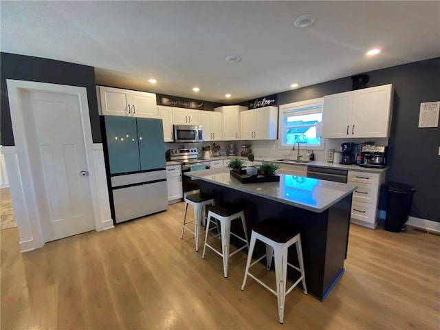 kitchen with stainless steel appliances, a sink, white cabinets, a kitchen breakfast bar, and a center island