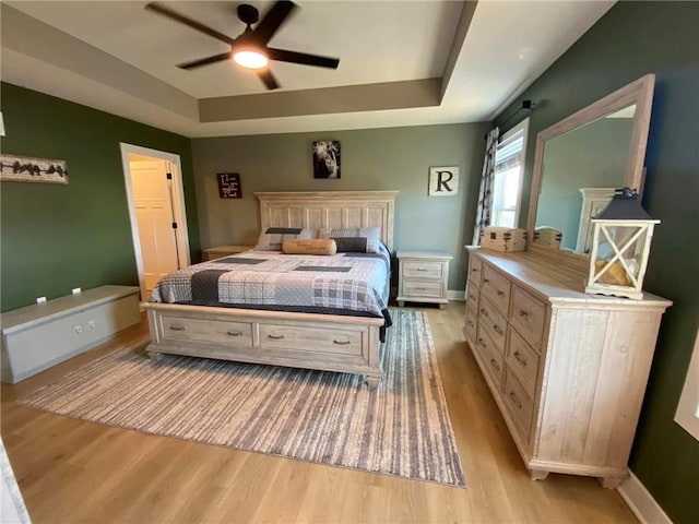 bedroom with light wood-style floors, baseboards, a tray ceiling, and ceiling fan