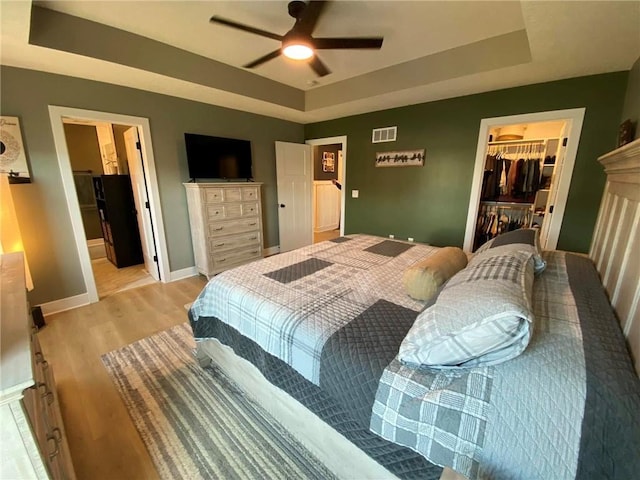 bedroom with a tray ceiling, visible vents, light wood-style flooring, a spacious closet, and baseboards