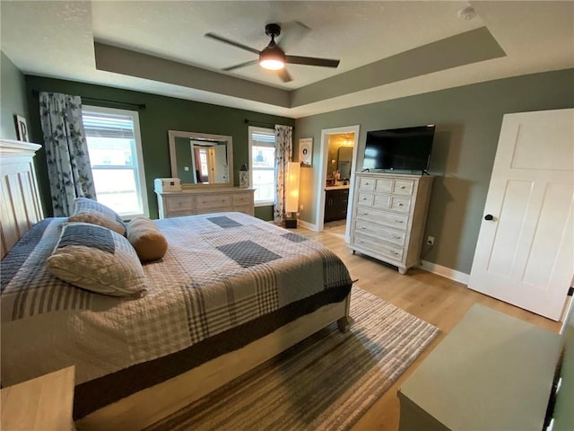 bedroom featuring light wood-type flooring, a raised ceiling, connected bathroom, and baseboards