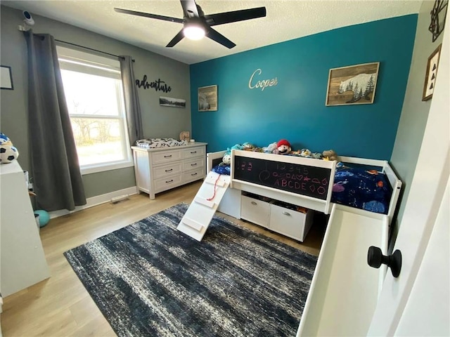 bedroom featuring ceiling fan, a textured ceiling, baseboards, and wood finished floors