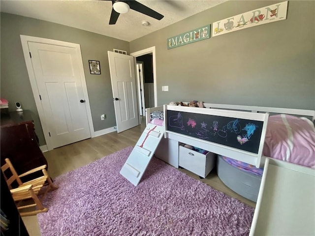 bedroom featuring a ceiling fan, visible vents, baseboards, and wood finished floors