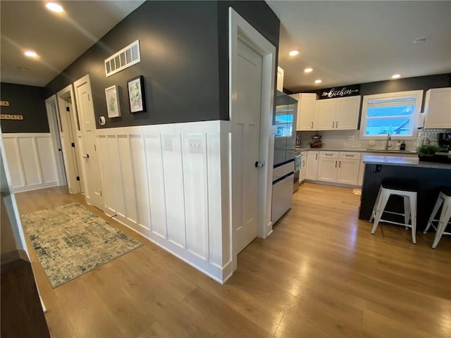 kitchen with a wainscoted wall, a sink, visible vents, light wood-style floors, and white cabinetry