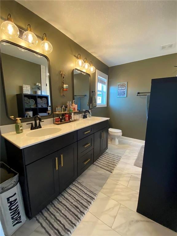 bathroom with marble finish floor, double vanity, a sink, and toilet