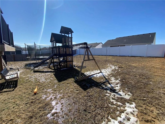 communal playground featuring a trampoline and a fenced backyard