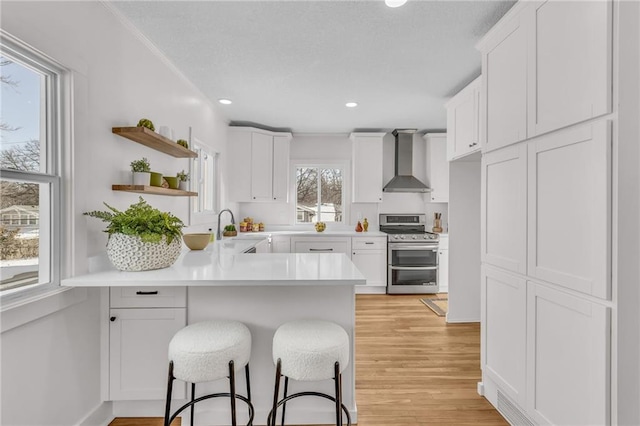 kitchen with range with two ovens, white cabinets, light countertops, wall chimney exhaust hood, and a kitchen bar