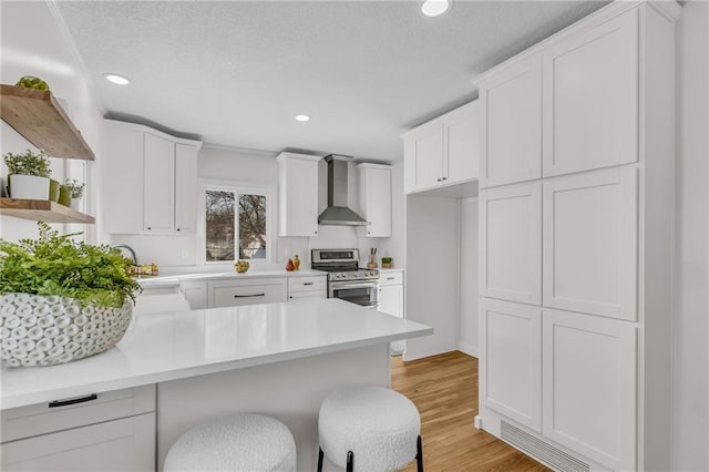 kitchen with a kitchen breakfast bar, white cabinets, light countertops, stainless steel range with electric cooktop, and wall chimney exhaust hood