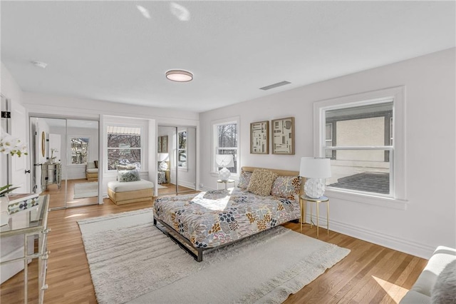 bedroom with baseboards, wood finished floors, visible vents, and multiple closets