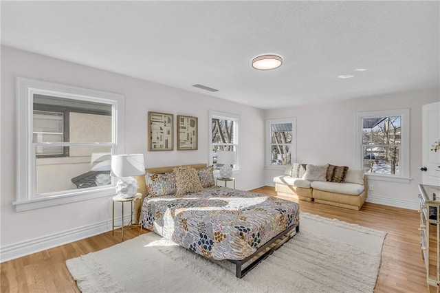 bedroom with baseboards, visible vents, light wood finished floors, and multiple windows