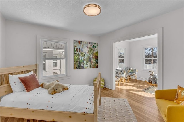 bedroom featuring a textured ceiling, light wood-style flooring, and baseboards