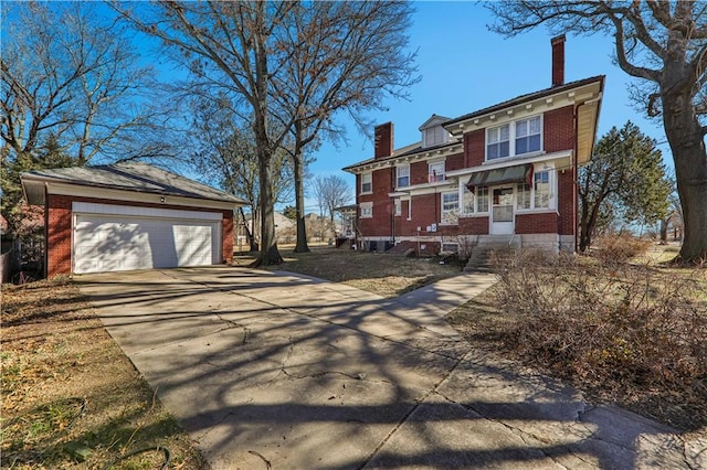 view of front facade featuring an outbuilding, concrete driveway, brick siding, and a chimney