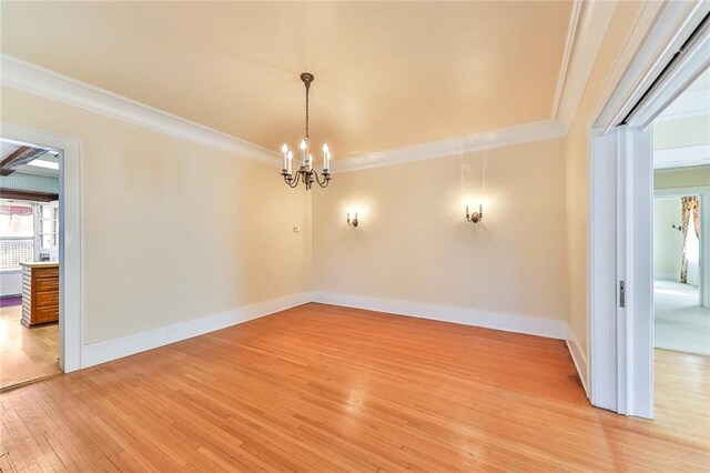 unfurnished room with a notable chandelier, baseboards, light wood-style flooring, and crown molding