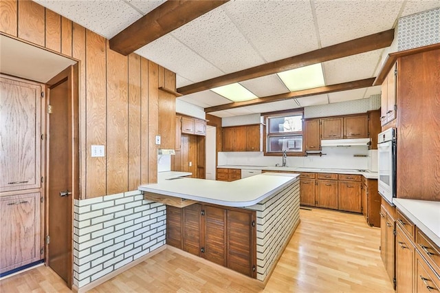 kitchen with brown cabinets, light wood-style floors, white appliances, a peninsula, and under cabinet range hood