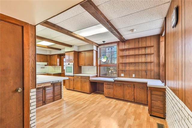 kitchen featuring brown cabinetry, built in study area, light wood-style flooring, oven, and light countertops