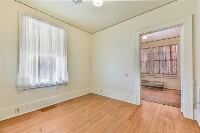 spare room with light wood-style floors, a wealth of natural light, visible vents, and baseboards