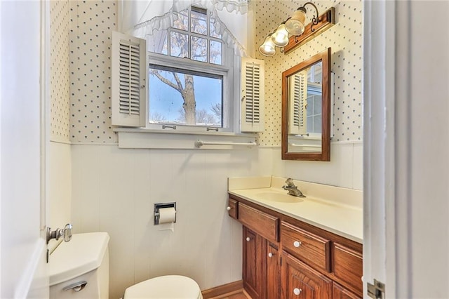 bathroom with vanity, toilet, and wallpapered walls