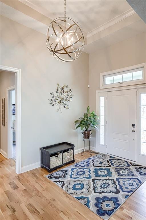 foyer with ornamental molding, light wood finished floors, a chandelier, and baseboards