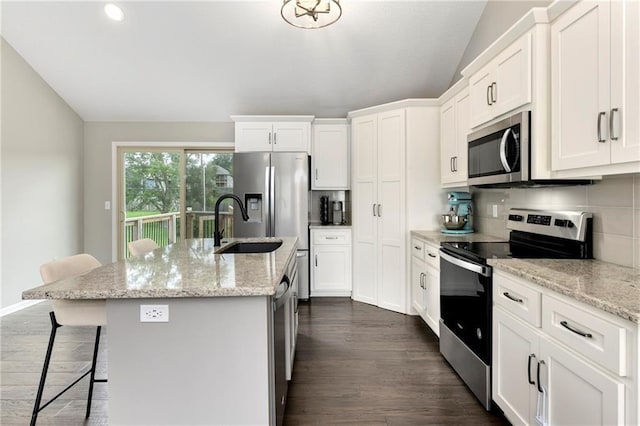 kitchen featuring a breakfast bar area, white cabinets, appliances with stainless steel finishes, light stone countertops, and an island with sink