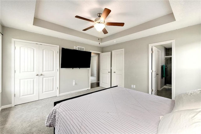 carpeted bedroom featuring a raised ceiling, baseboards, and ensuite bathroom