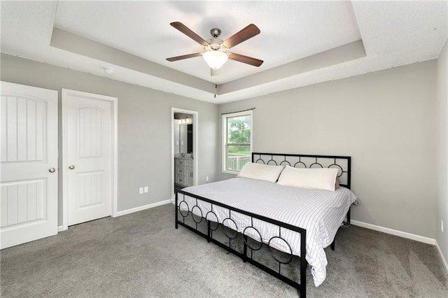 carpeted bedroom with ensuite bath, a raised ceiling, and baseboards