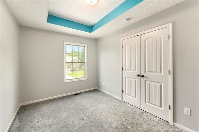 unfurnished bedroom featuring a textured ceiling, baseboards, a raised ceiling, and carpet flooring