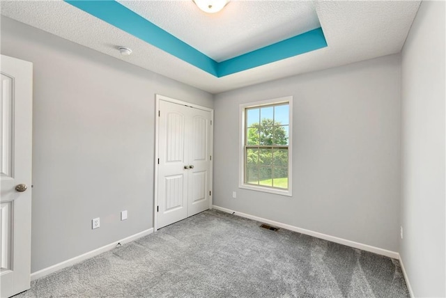 empty room featuring a textured ceiling, light carpet, visible vents, baseboards, and a raised ceiling