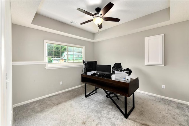 office area featuring light carpet, visible vents, baseboards, a ceiling fan, and a tray ceiling