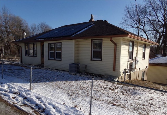 view of snow covered exterior featuring cooling unit, fence, and roof mounted solar panels