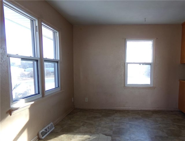 empty room featuring a wealth of natural light, visible vents, and baseboards