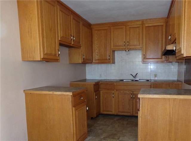 kitchen featuring brown cabinets, a sink, backsplash, and exhaust hood