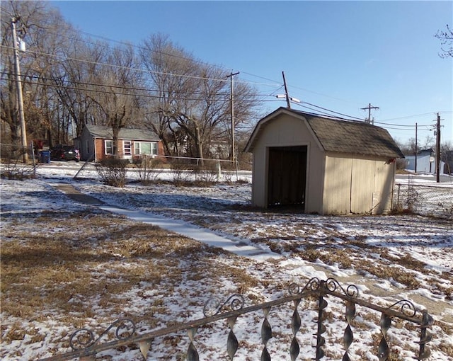 snow covered structure featuring a storage shed, fence, and an outbuilding